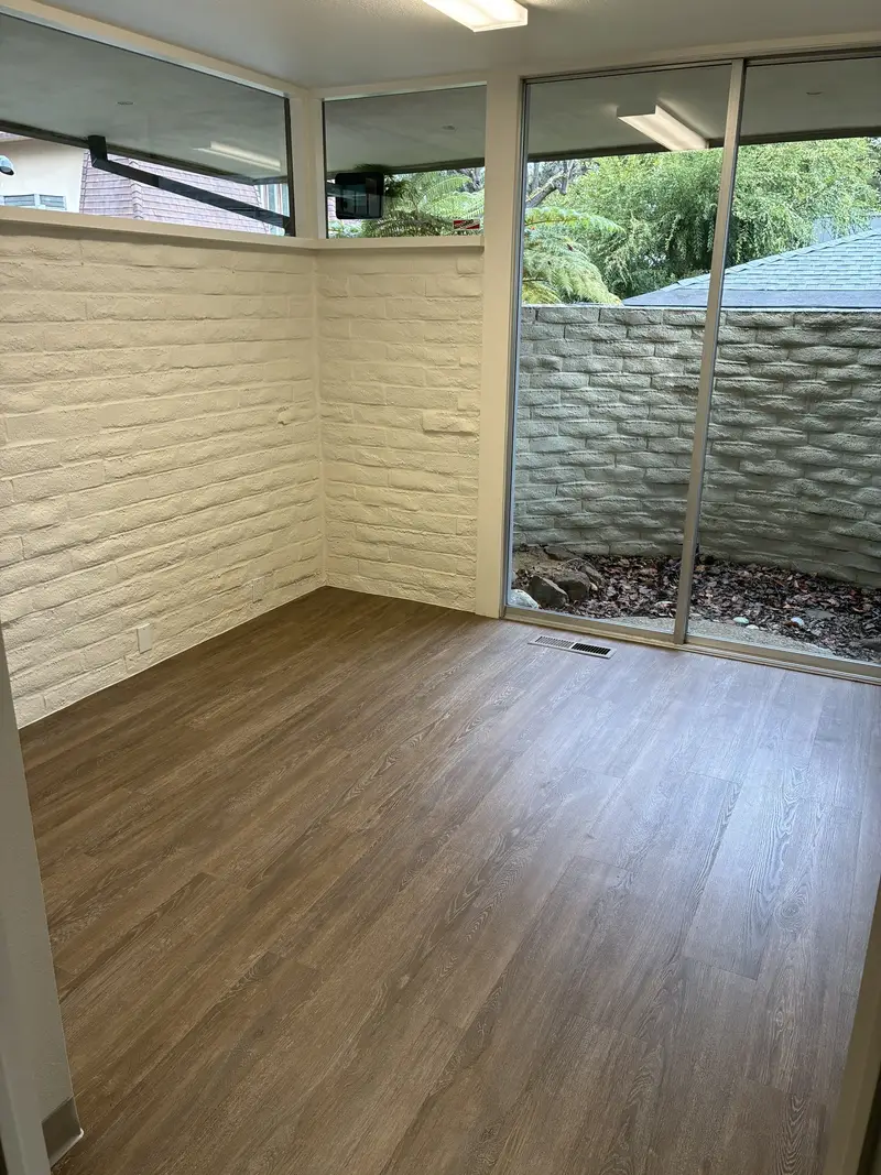 An empty room with a white brick wall and large windows, before the sound booth is installed