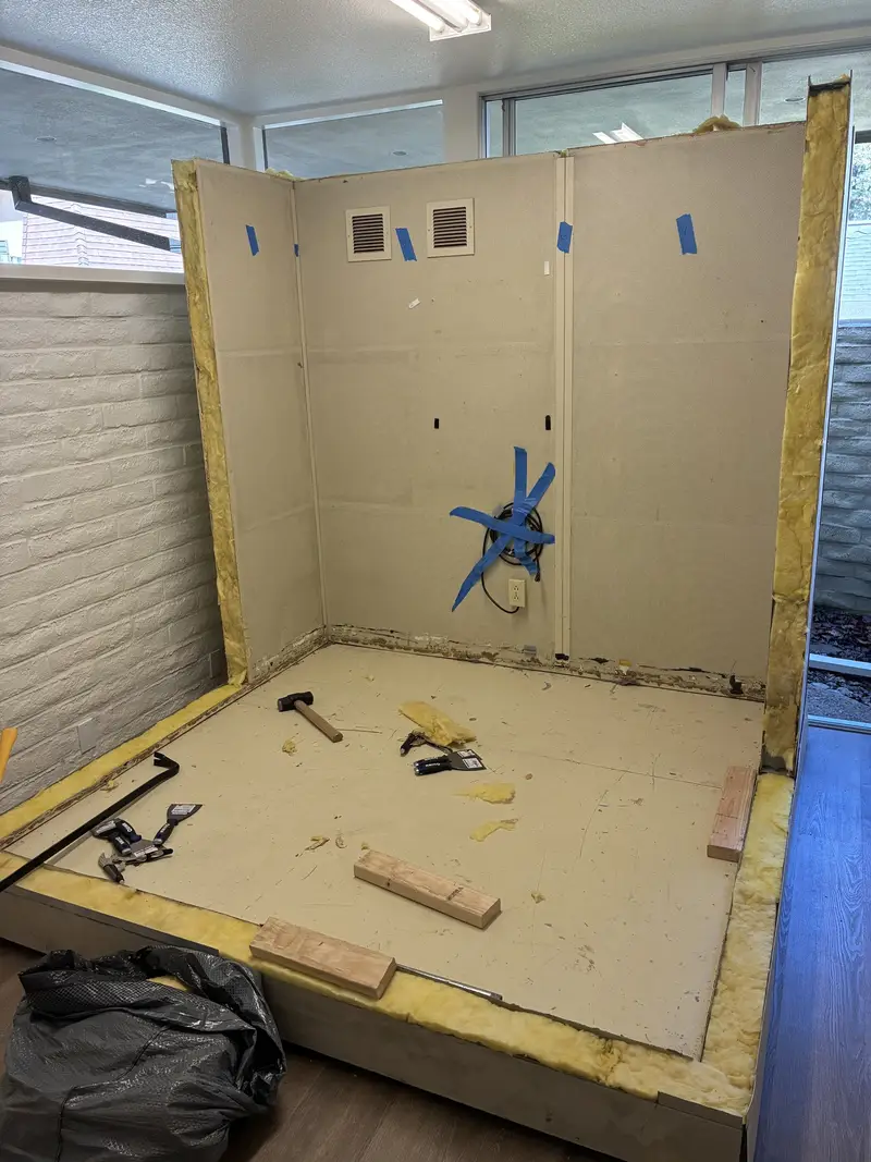 The floor and two wall panels of a sound booth set in place, with tools on the booth floor