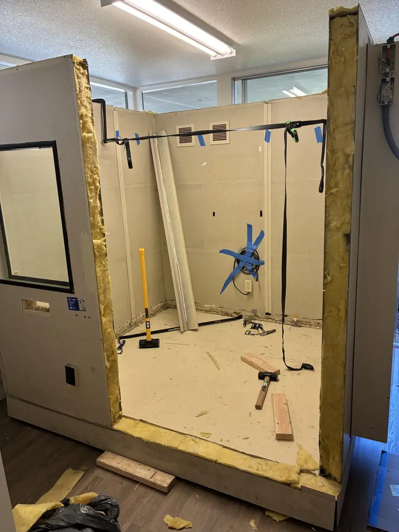 A sound booth partly assembled, with the window panel installed and straps holding the walls square