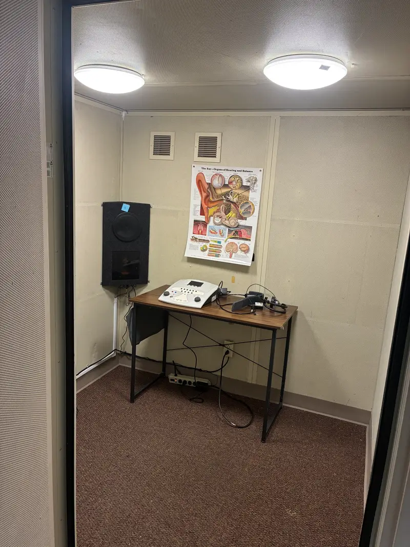 The finished interior of a rebuilt sound booth with an audiometer on a desk, a wall speaker, and overhead lights on